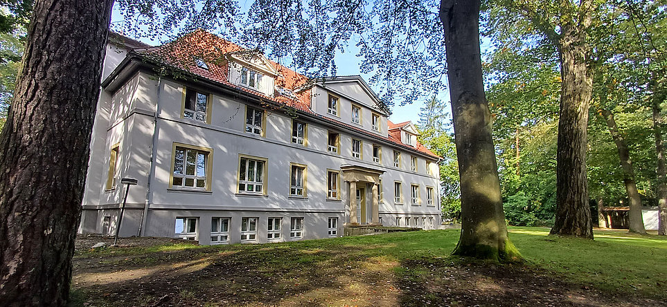 Mehrstöckiges weißes Haus mit Säulenportal im bewaldeten Hagen