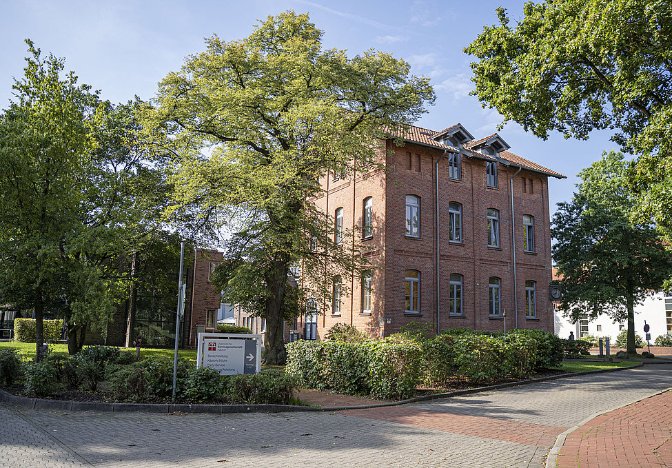 Rotes Backsteingebäude mit Bäumen und Orientierungsschild