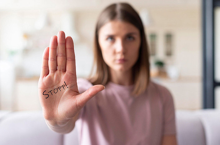 Frau hält Hand mit dem klar lesbaren Schriftzug STOPP in die Kamera