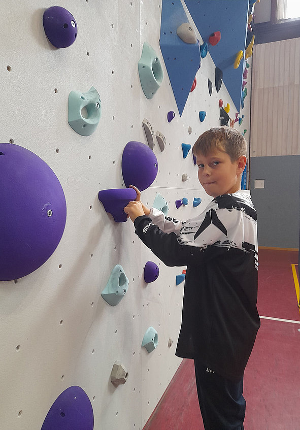 Junge an Kletterwand greift einen lila Griff