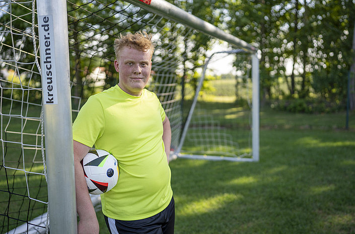 Jugendlicher lehnt am Fußballtor mit Ball unter dem Arm