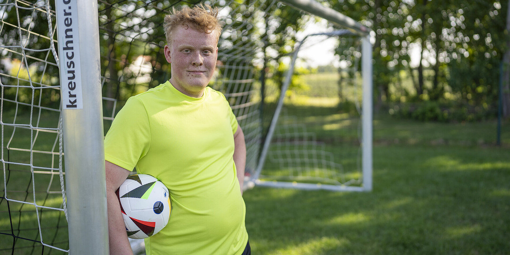Jugendlicher lehnt am Fußballtor mit Ball unter dem Arm