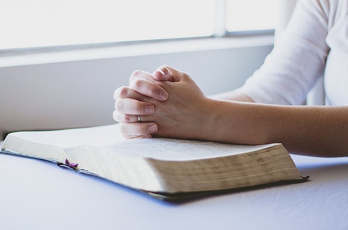 Gefaltete Hände auf einer offenen Bibel