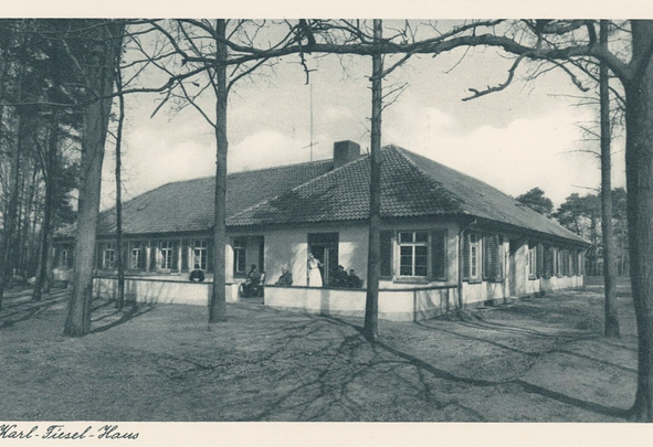 Karl-Fiesel-Haus eingeschossiges Gebäude mit Veranda und sitzenden Personen