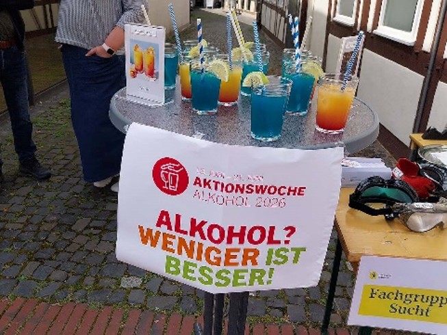 Ein Informationsstand mit bunten Getränken und einem Banner mit der Aufschrift "Alkohol? Weniger ist besser!"